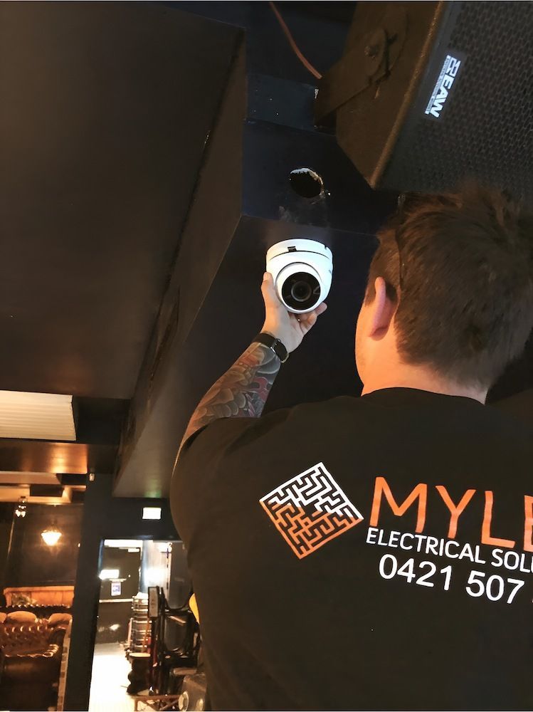 A Man Wearing a Myle Electrical Shirt is Holding a Camera — Mylec Electrical Solutions in North Wollongong, NSW