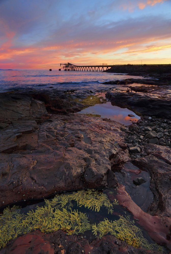 A Sunset Over a Rocky Beach With a Boat in the Distance — Mylec Electrical Solutions in Shell Cove, NSW