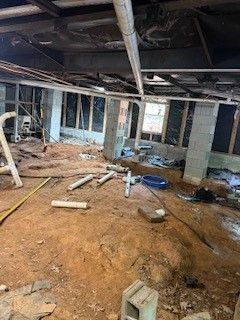 Unfinished basement with exposed beams, concrete columns, dirt floor, and construction debris scattered around.