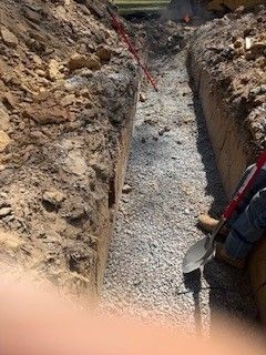 Narrow gravel trench with dirt walls and a worker holding a shovel on the right side
