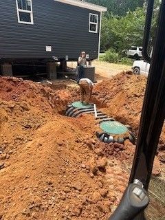 Backyard excavation with two septic tank covers beside a dark house and dirt pile