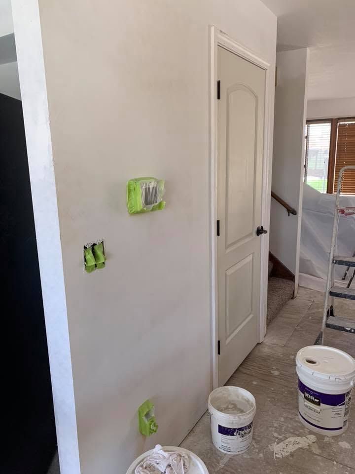 Interior hallway with white doors, green tape on outlets, and paint buckets on the floor during renovation