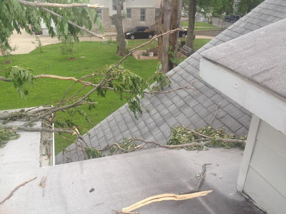 Tree branches fallen across a gray roof and lawn after storm damage.