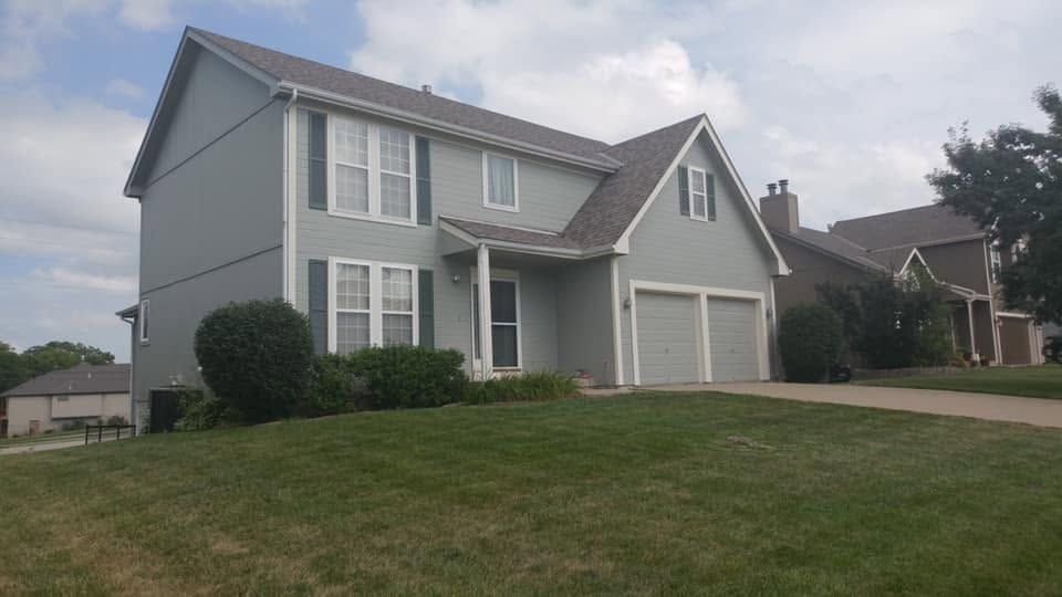 Two-story gray suburban house with a front lawn and driveway under a cloudy sky