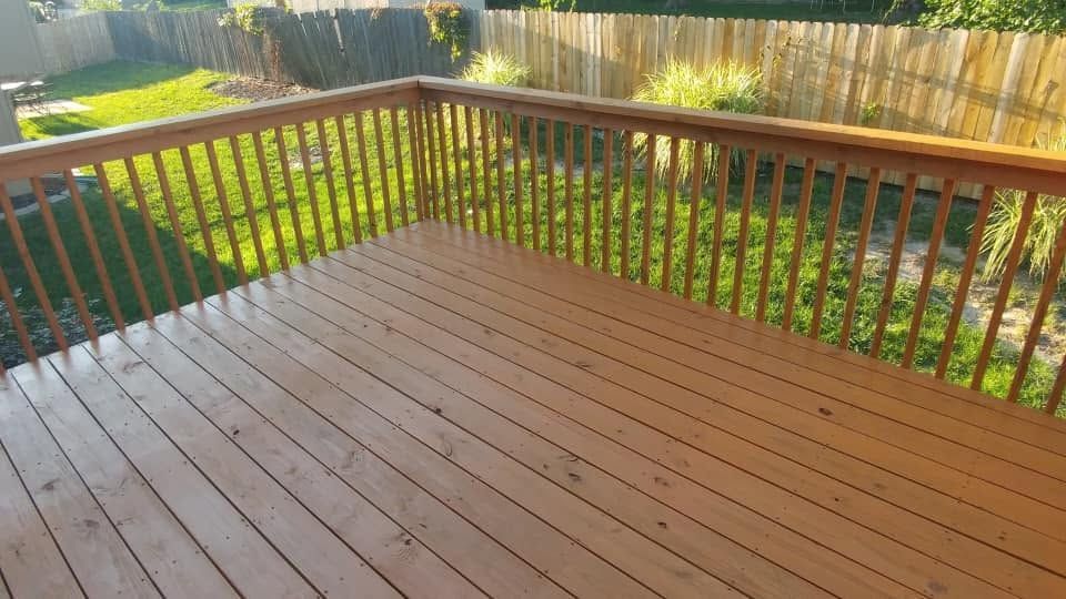 Wooden deck with railings overlooking a sunny green garden.
