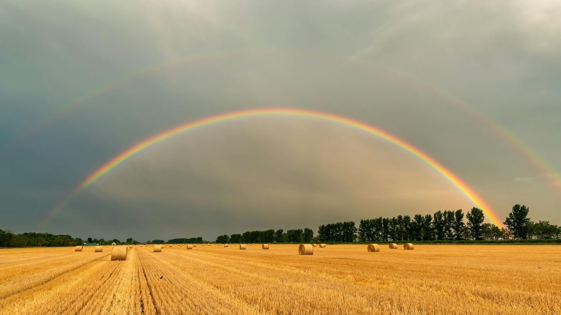 A rainbow is visible over a field of hay bales.