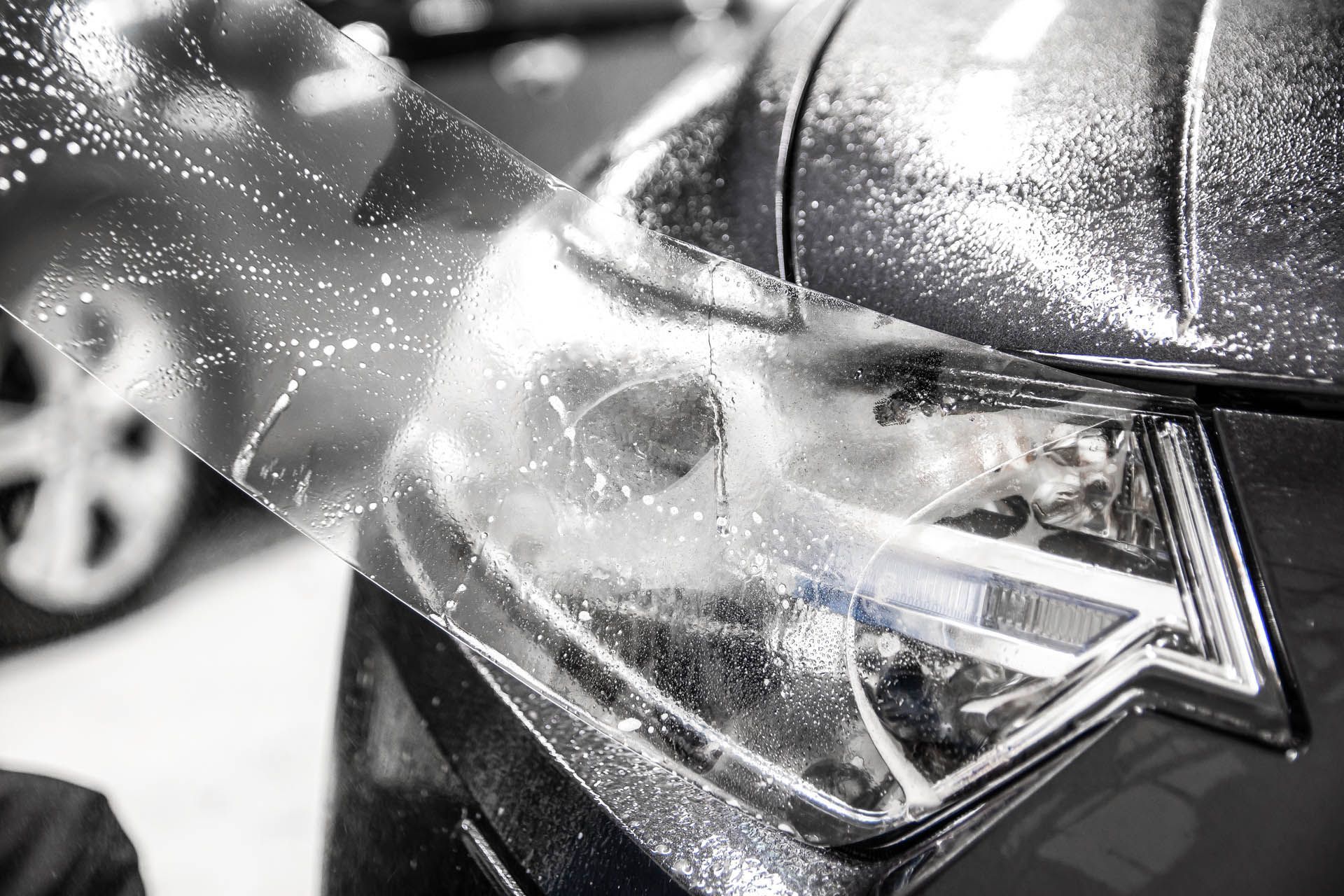 Close-up of a black car headlight being washed with water spray