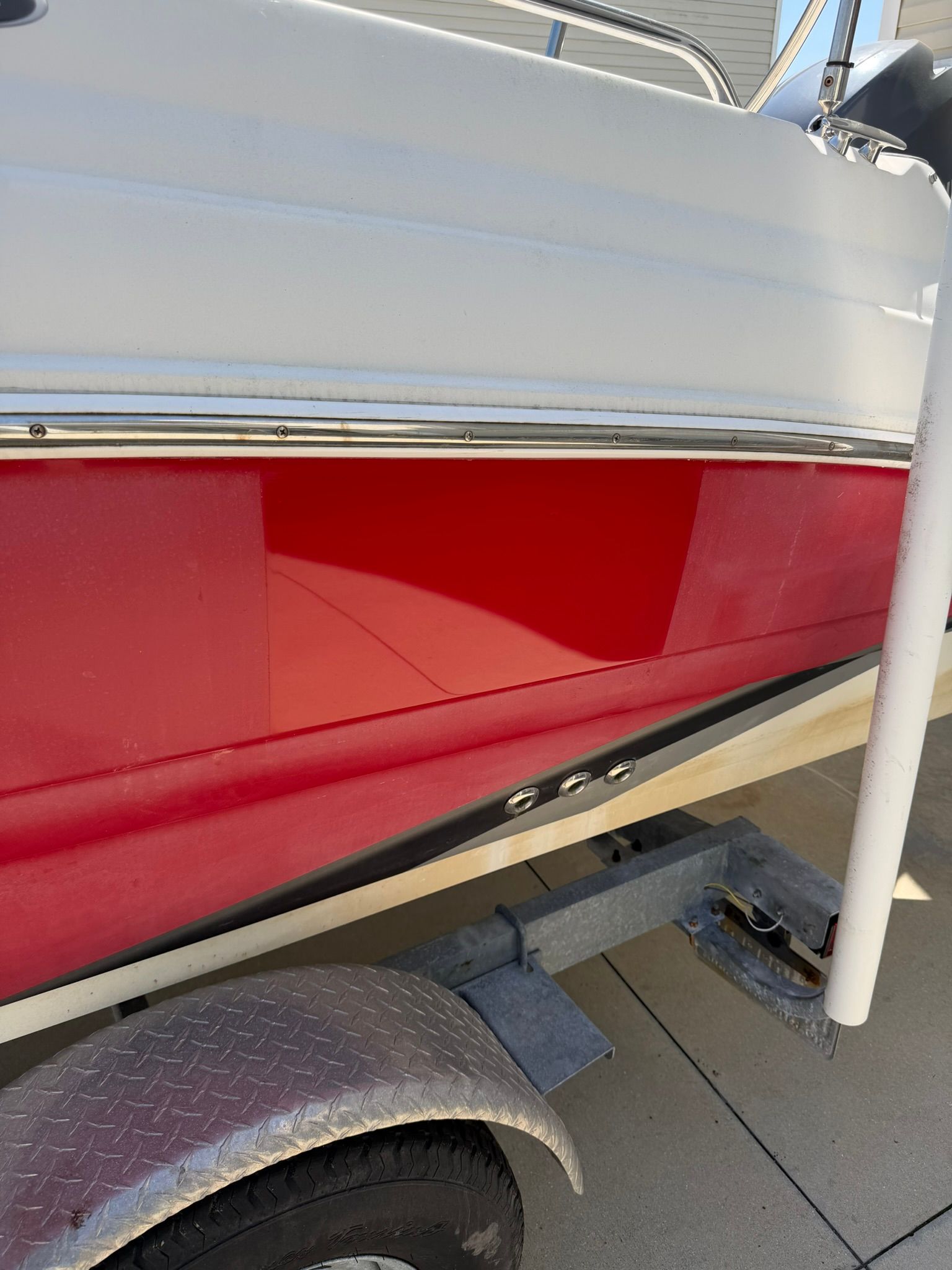 Red boat hull on a trailer with a gray fender and white support post, shown close-up.