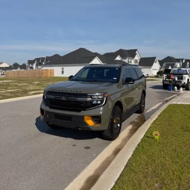 Dark gray pickup truck parked on a suburban street beside a curb, with houses in the background.