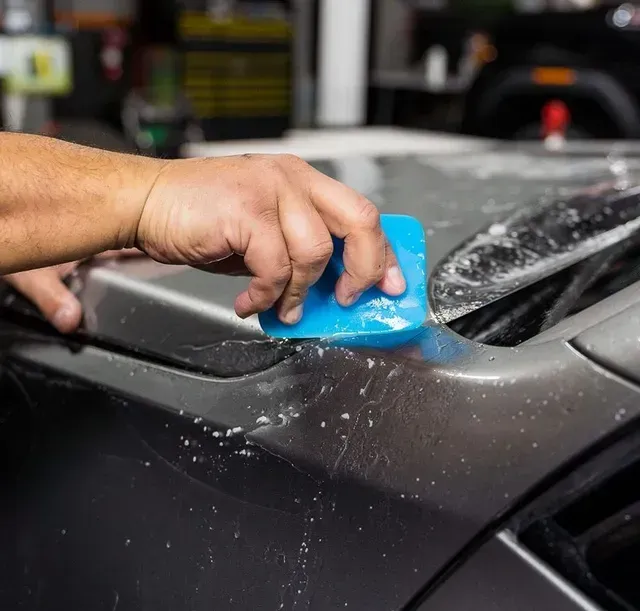 Hand wiping a gray car with a blue sponge, cleaning soap from the surface