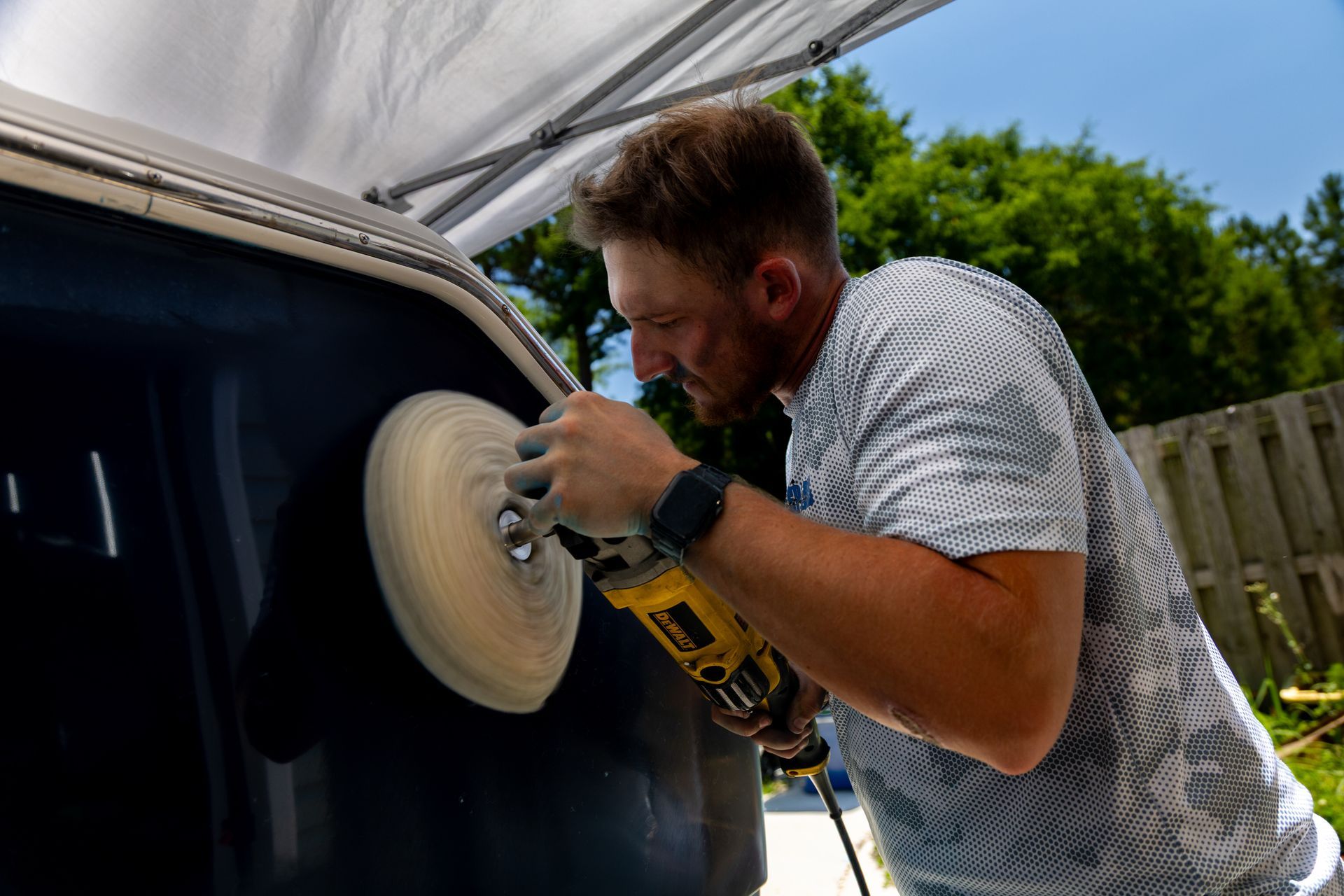 Man polishing a car door with a buffer outdoors under a canopy