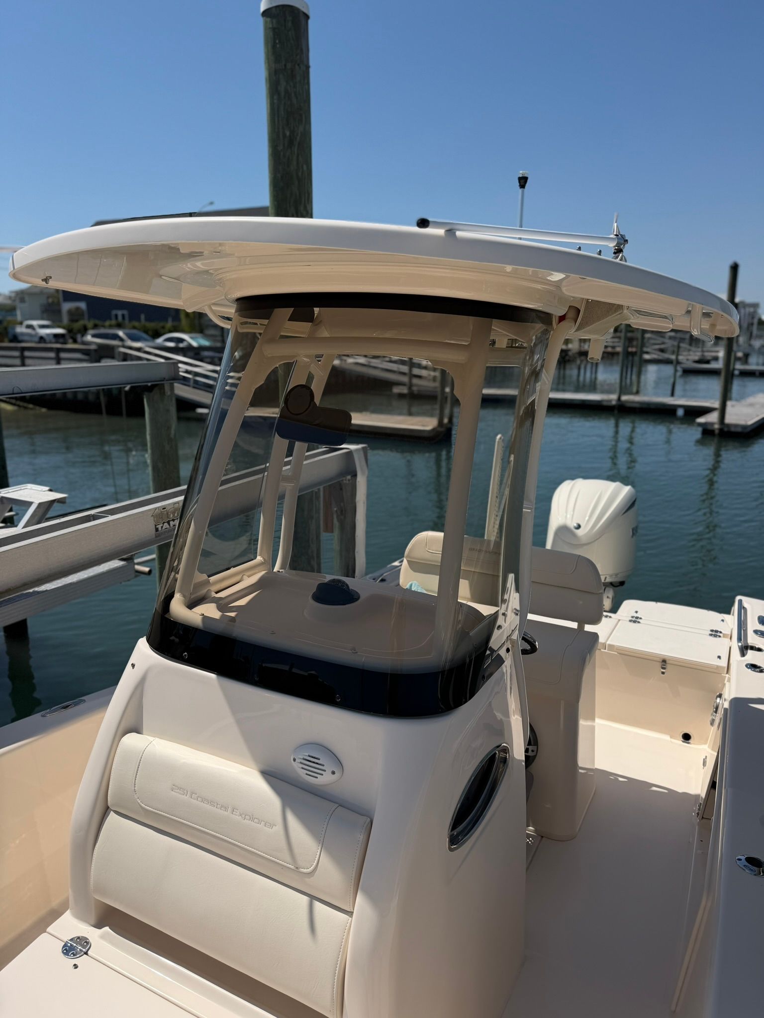 White center-console boat docked at a marina, with a T-top and blue water in the background