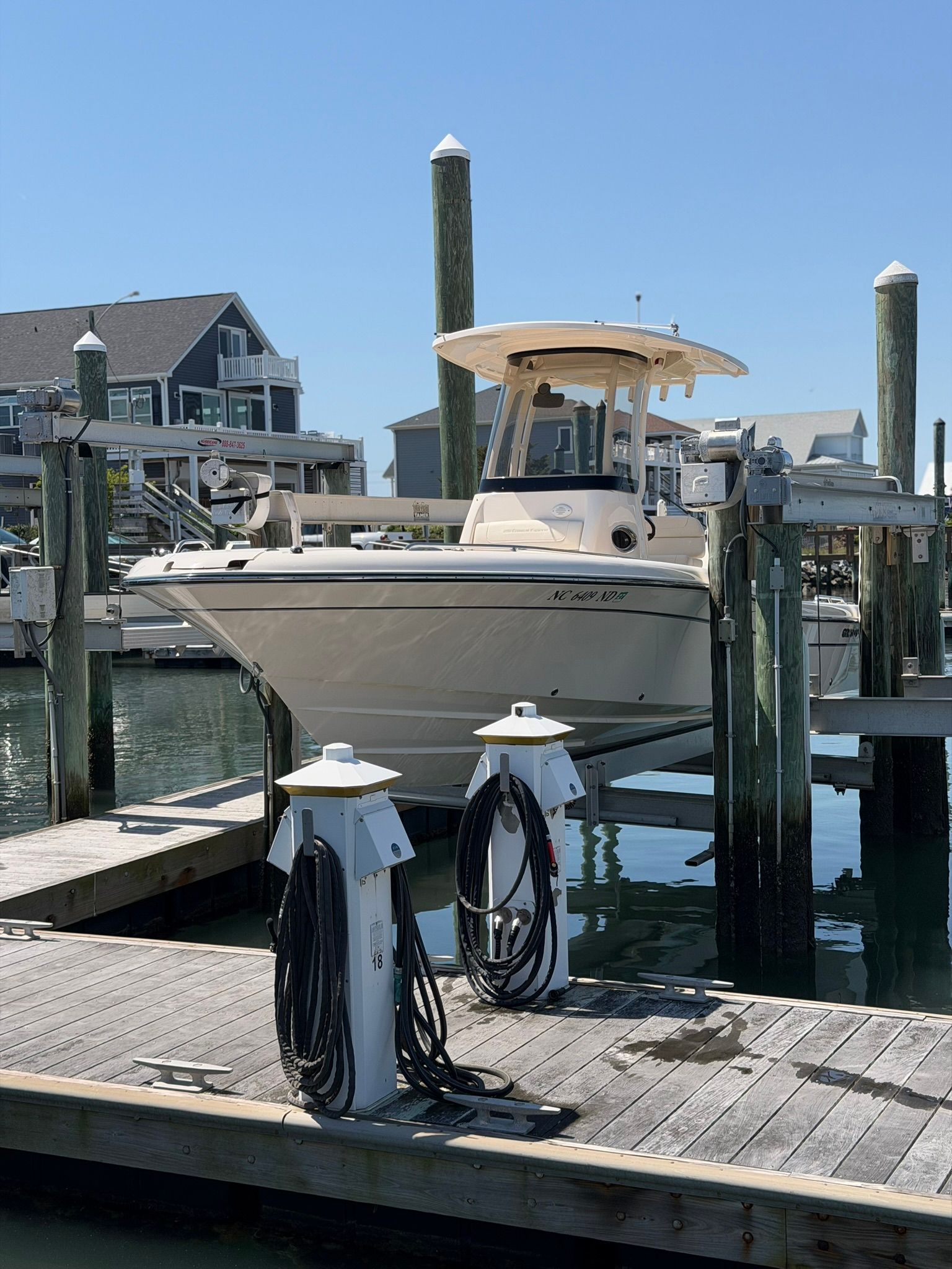 White boat docked at a marina with two bike racks on the wooden pier and houses in the background