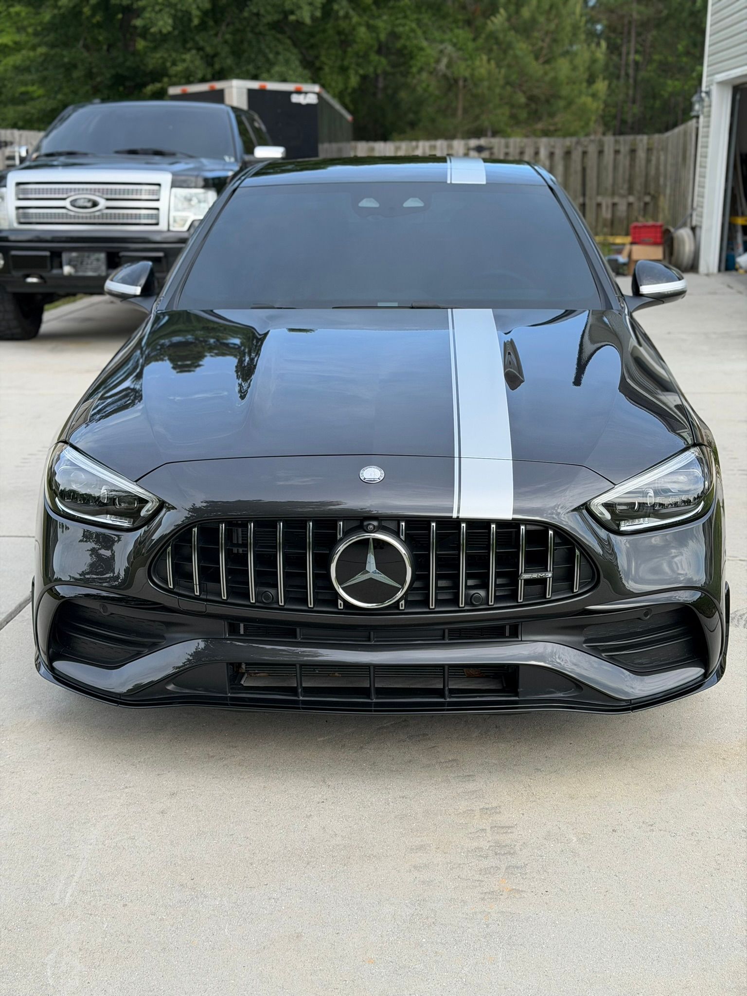 Black Mercedes sedan with a silver racing stripe parked in a driveway, front view