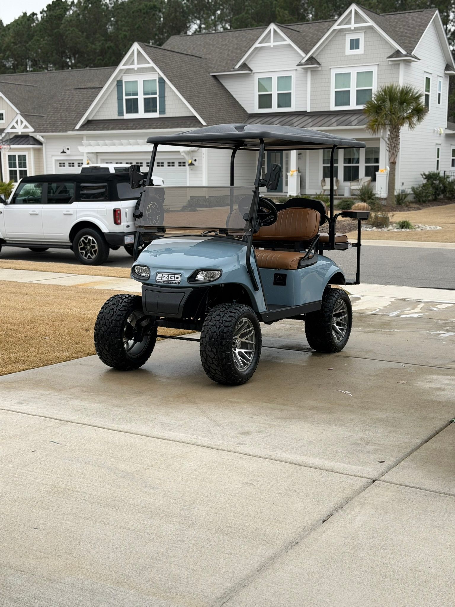 Blue golf cart parked on a suburban driveway in front of white houses and a pickup truck