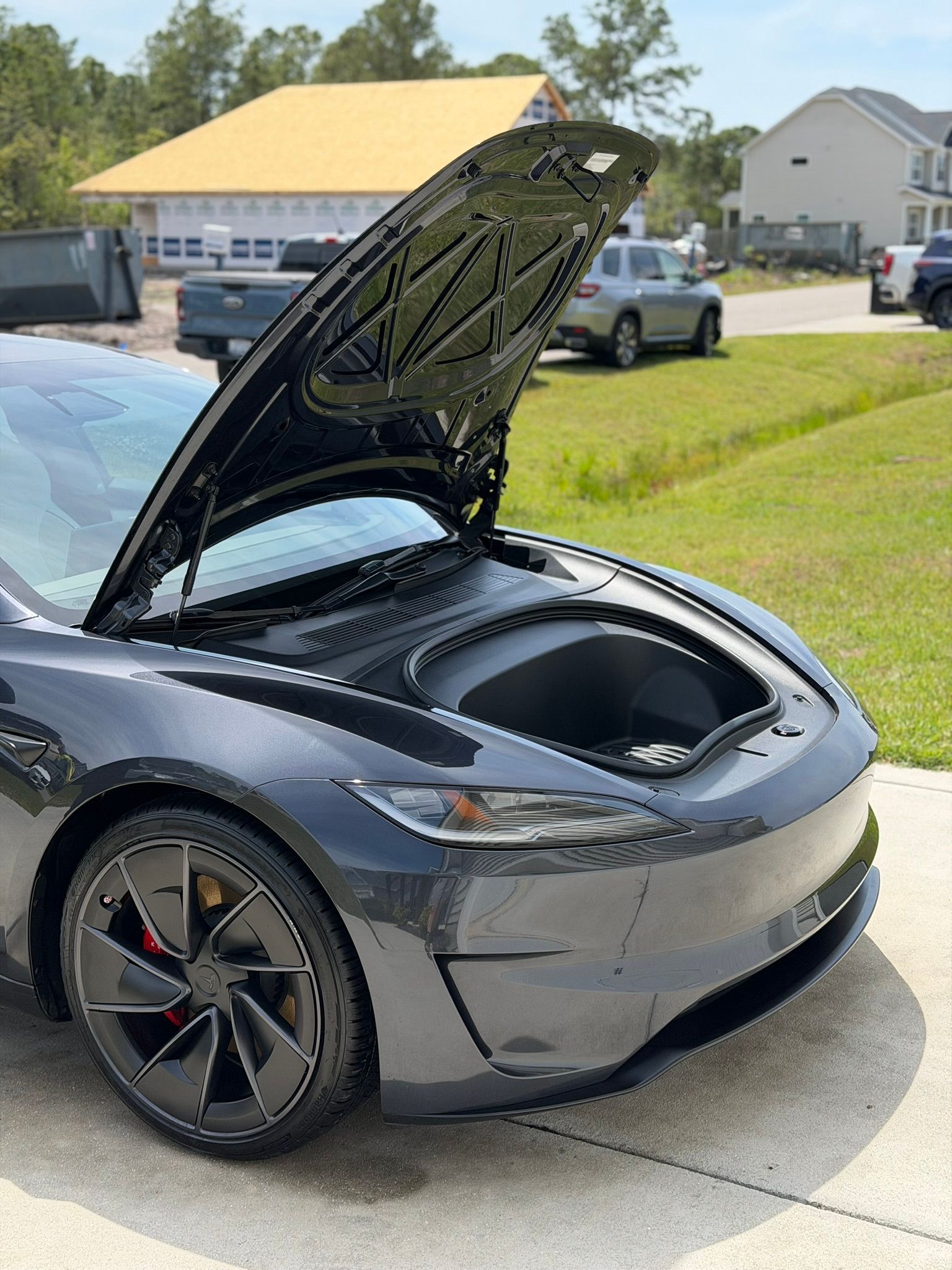Gray sports car with open rear hatch in a suburban driveway