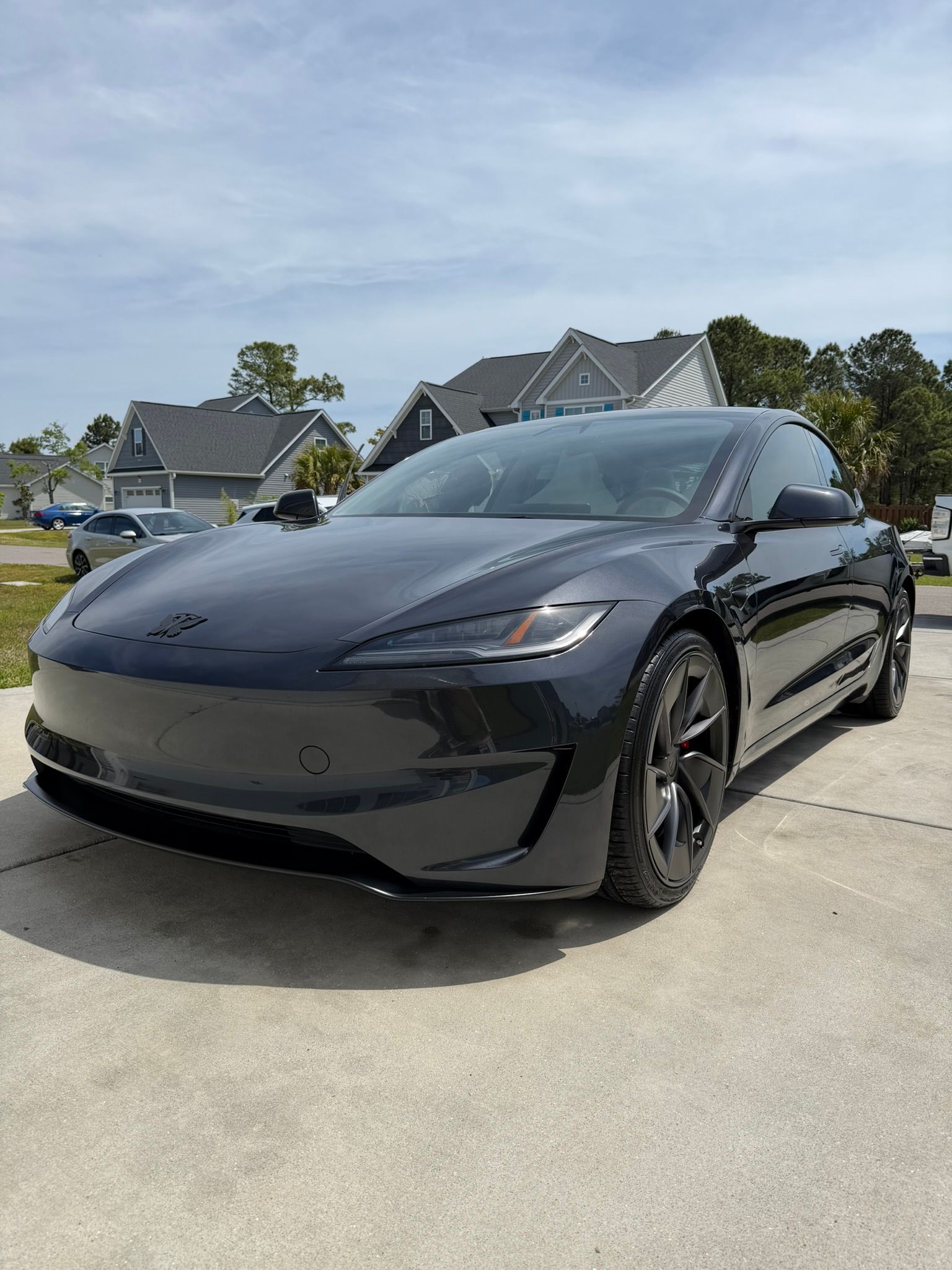 Black Tesla sedan parked on a driveway in a suburban neighborhood under a blue sky