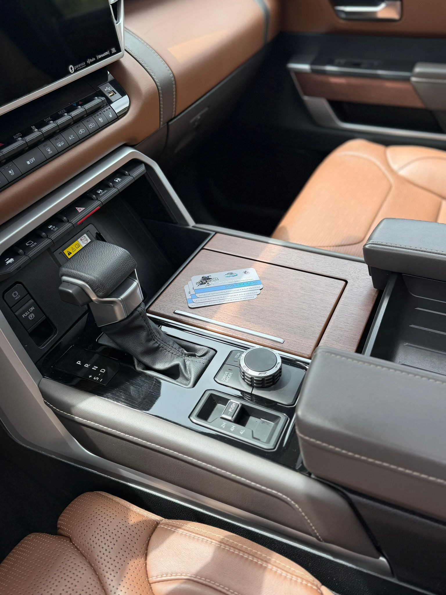 Luxury car center console with tan leather seats, cupholder, storage compartment, and control knob