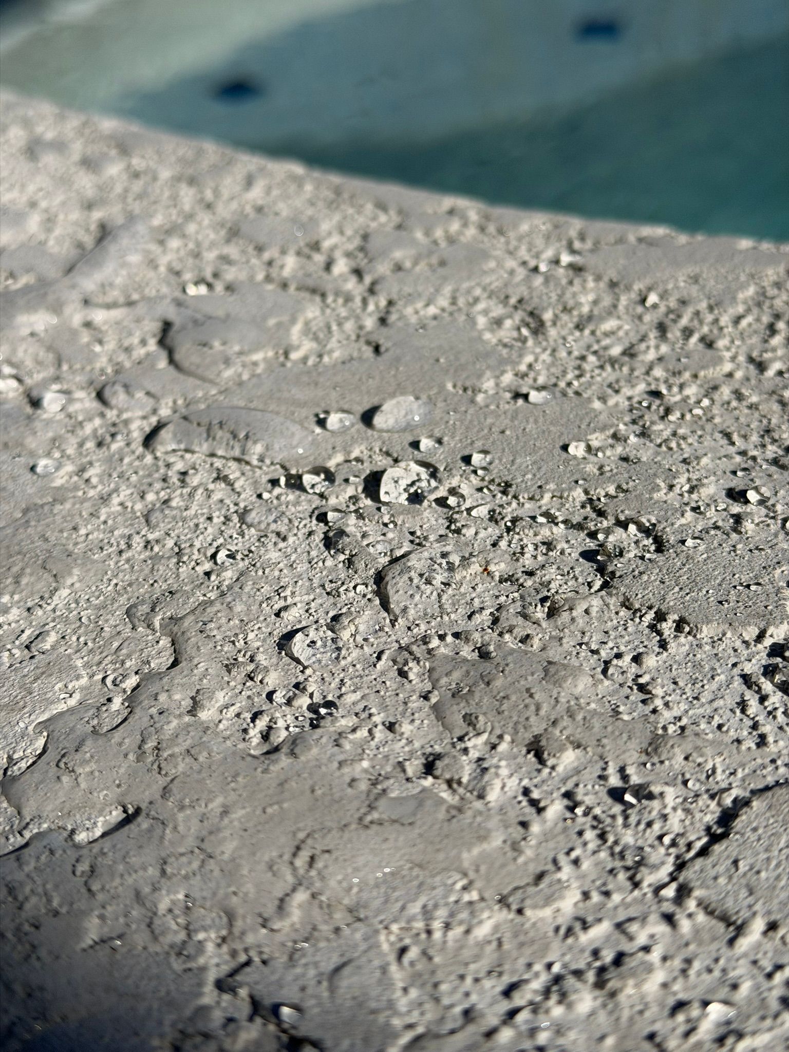 Close-up of rough gray concrete edge beside blue pool water
