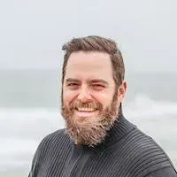 Smiling bearded man in a dark sweater outdoors by the sea