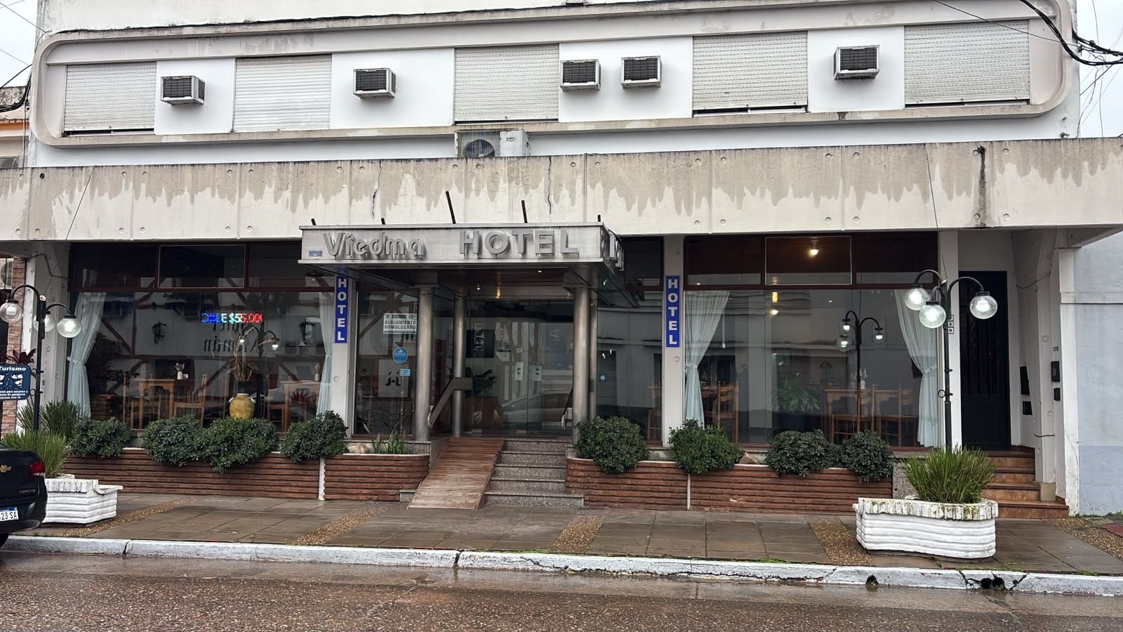 Dos personas con mochilas entran en un hotel situado en una acera de la ciudad al anochecer.