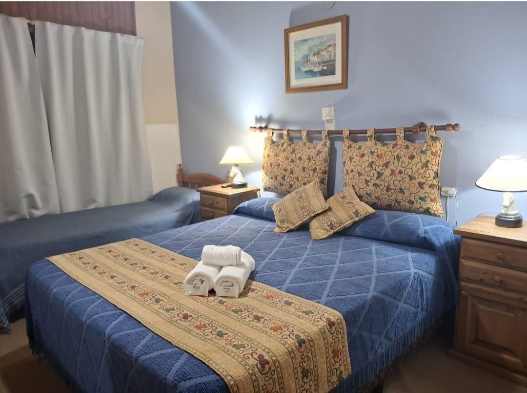 Habitación de hotel moderna con cama, escritorio y zona de estar, iluminación cálida y mostrador de recepción cerca de las ventanas.