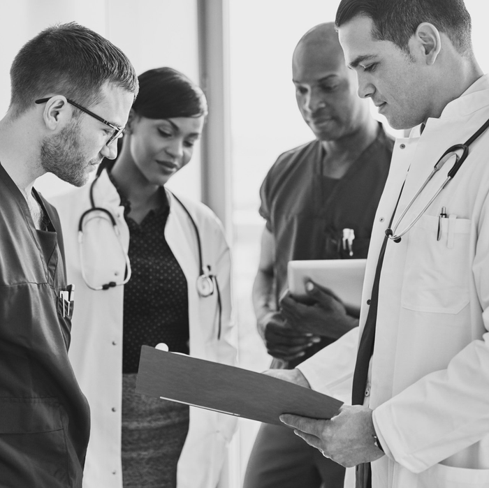 A group of doctors are looking at a clipboard in a black and white photo.