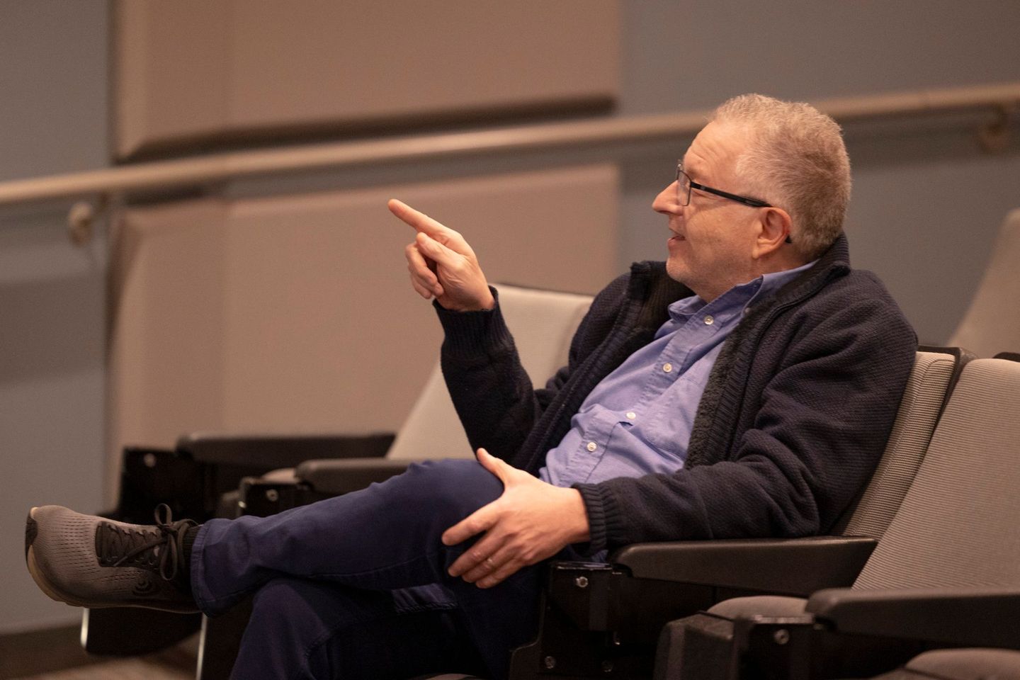 A man is sitting in a chair in an auditorium talking to someone.