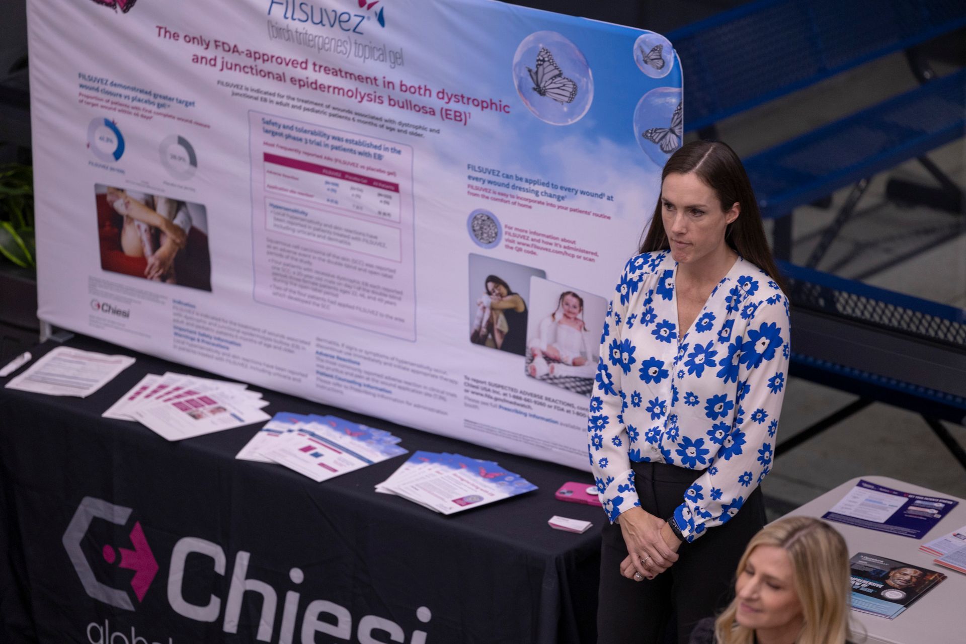 Two women are standing in front of a poster on a table.