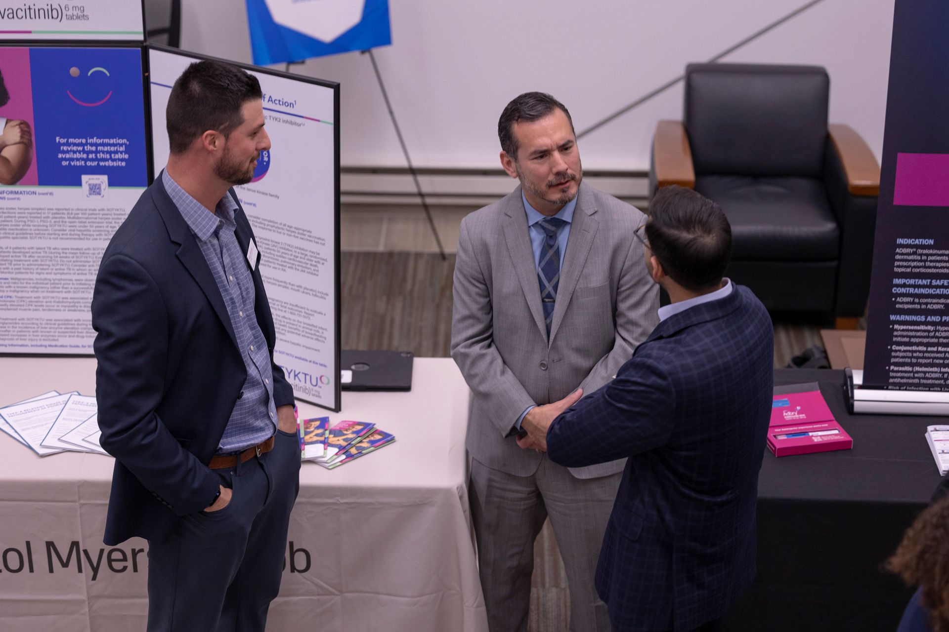 Three men in suits are standing around a table talking to each other.