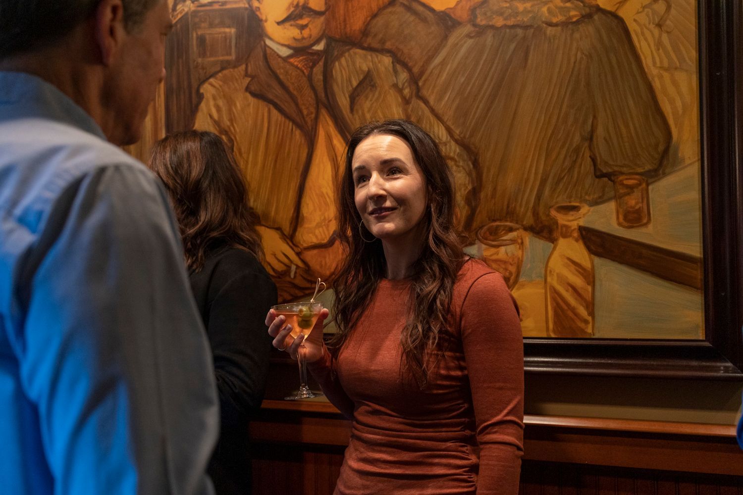 A woman is standing in front of a painting holding a glass of wine.