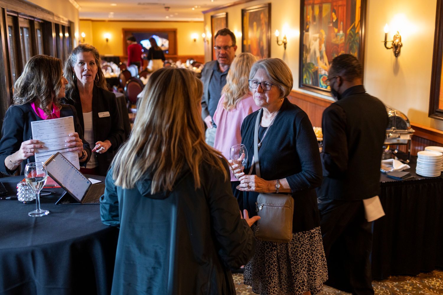 A group of people are standing around a table in a room talking to each other.
