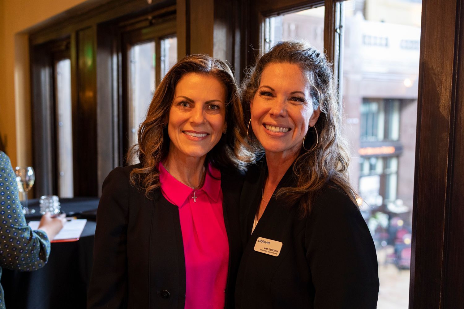 Two women are posing for a picture in front of a window.