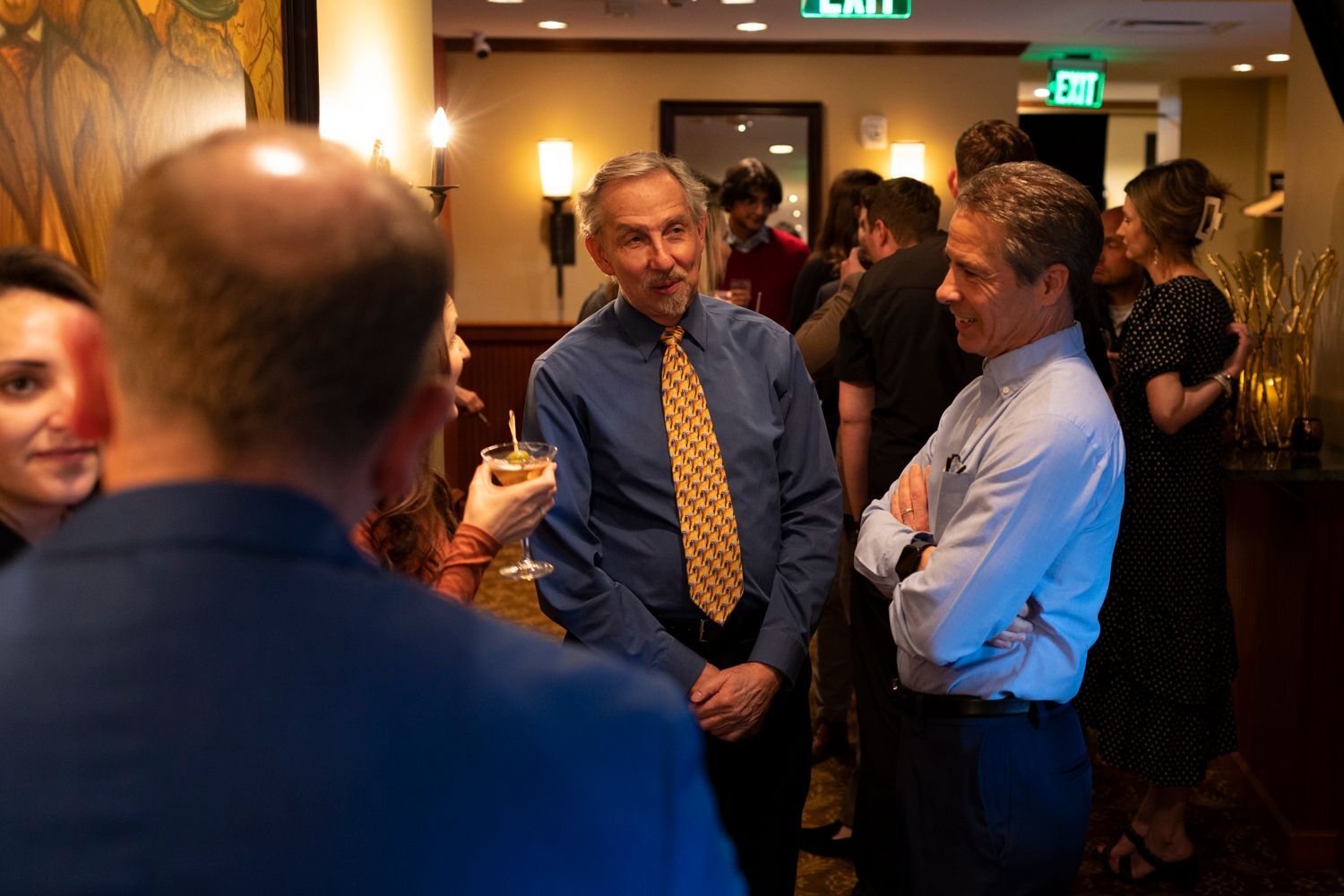 A group of people are standing in a room with an exit sign in the background.