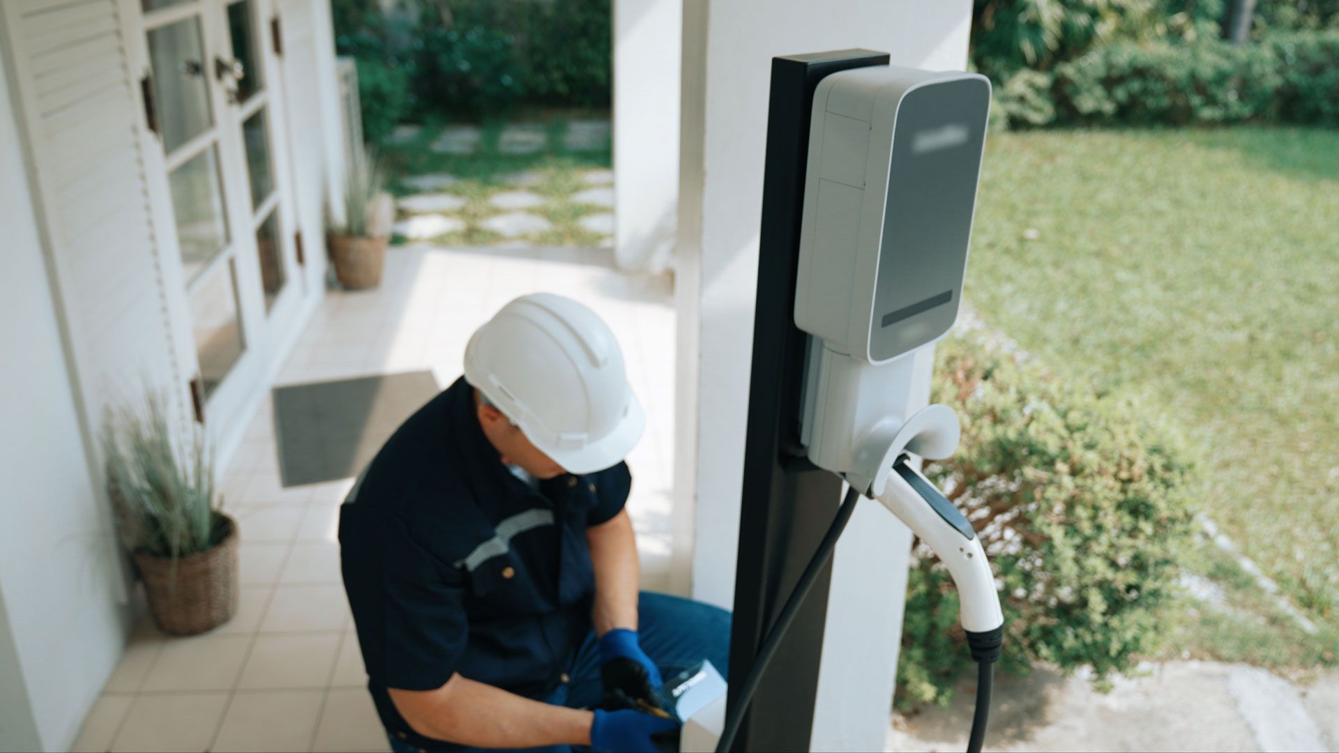 Technician in a hard hat installing an EV charger outside a house
