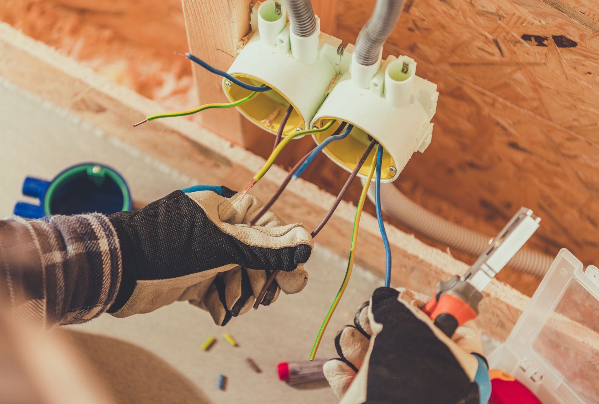 Gloved hands wiring two ceiling light fixtures with colorful cables in an unfinished room