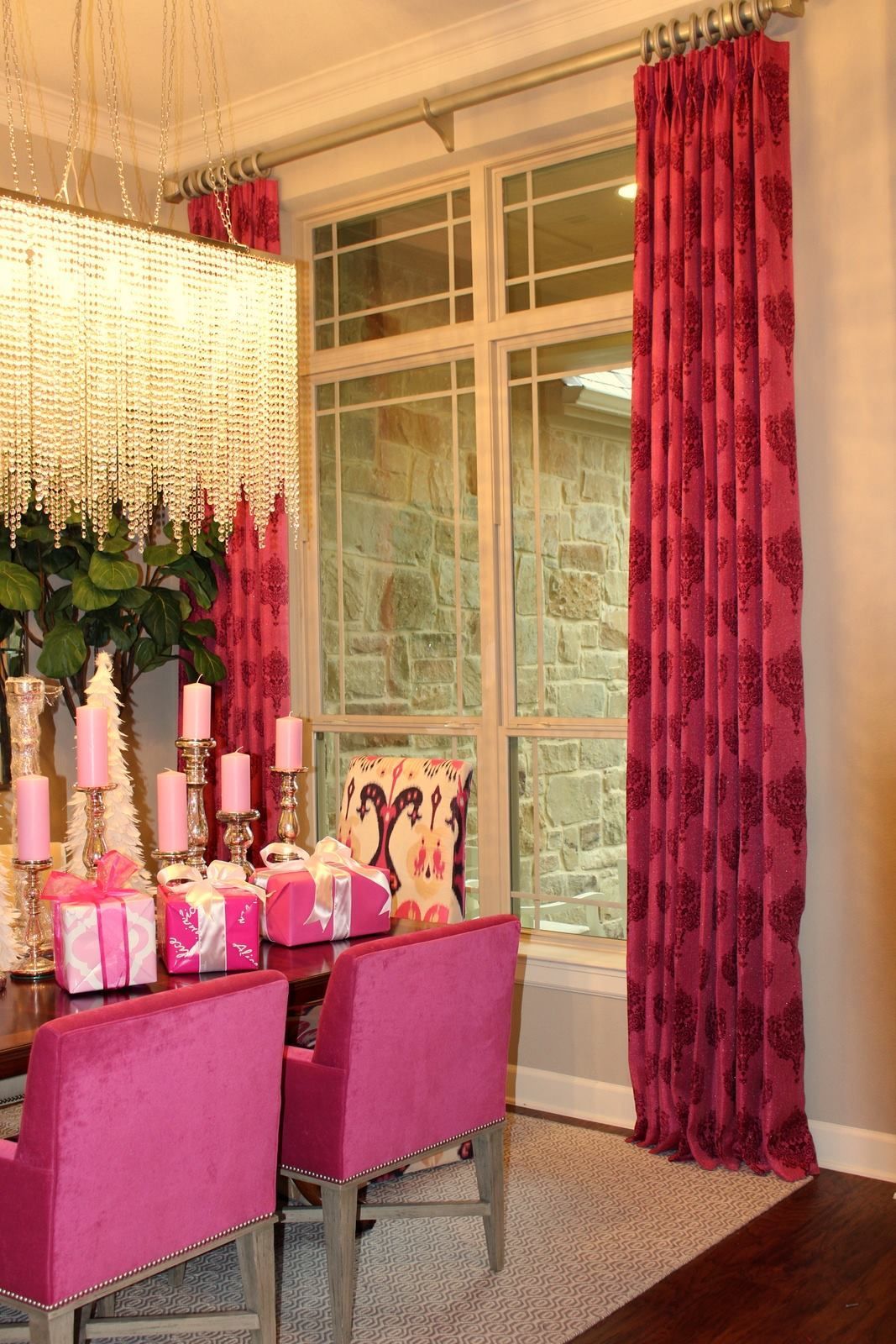 A dining room with pink chairs , a table and a chandelier.