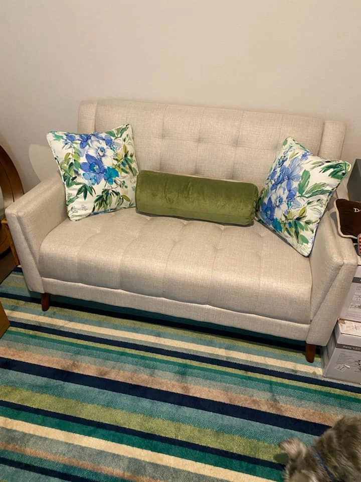 A white couch with blue and green pillows is sitting on a striped rug in a living room.