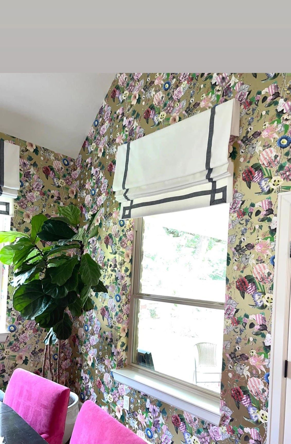 A room with a floral wallpaper and a window with a roman shade.