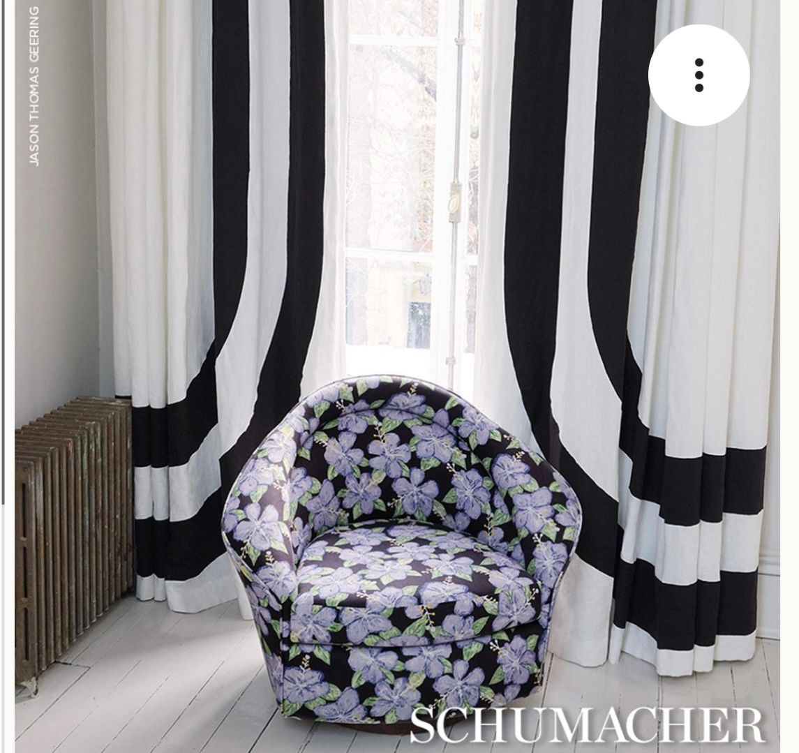 A chair with purple flowers on it sits in front of black and white curtains
