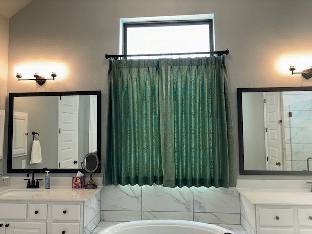 A bathroom with two sinks , two mirrors , a tub and a window.