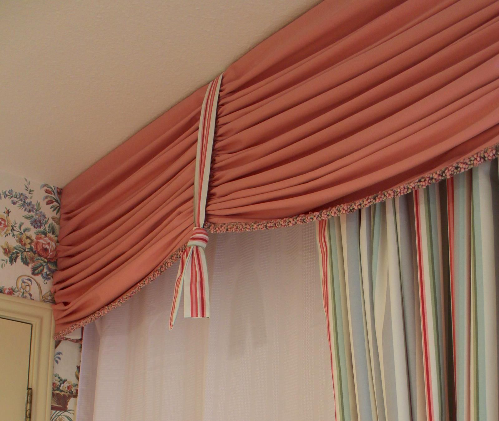 A pink curtain hangs over a window with striped curtains
