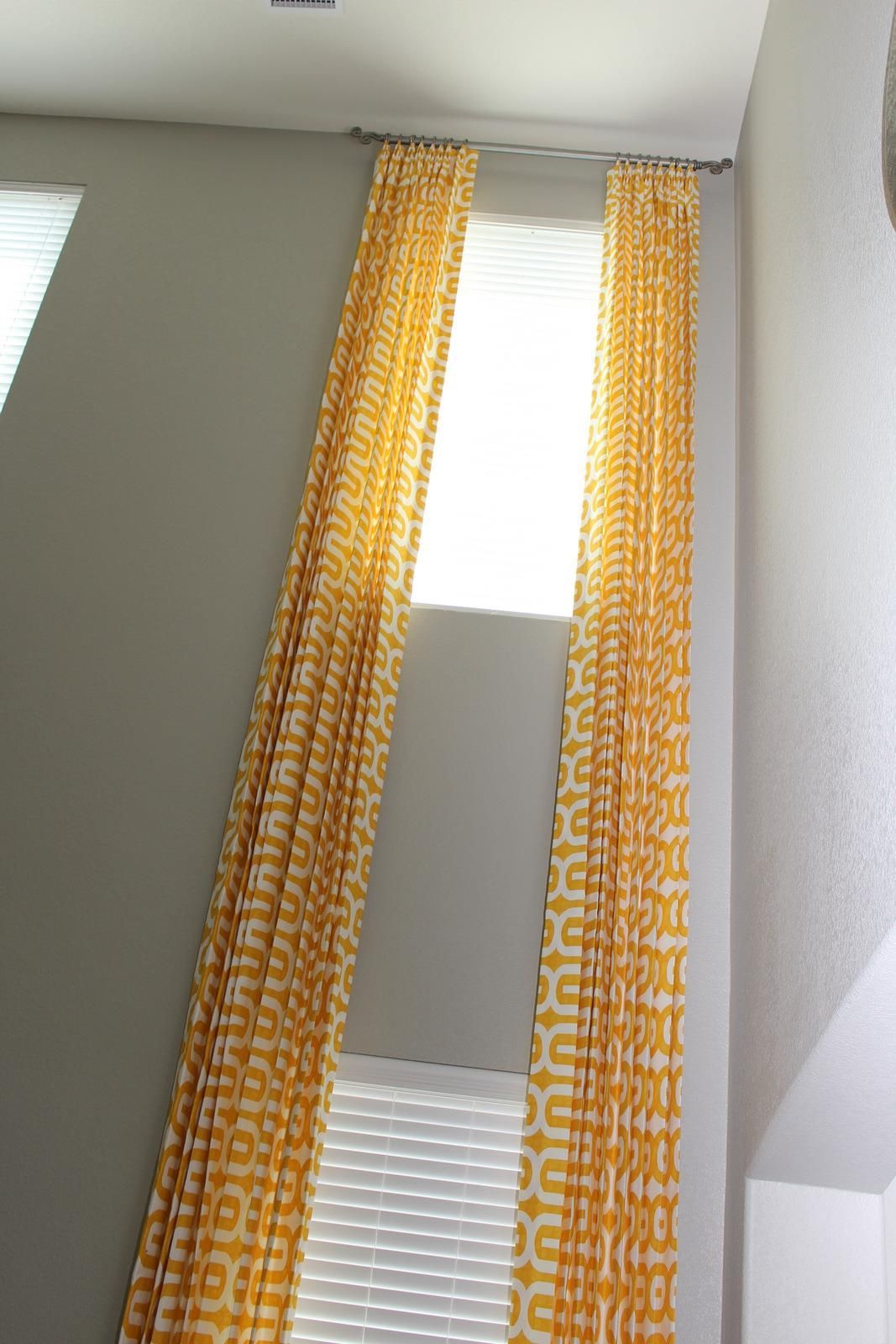 A pair of yellow curtains are hanging from the ceiling above two windows.
