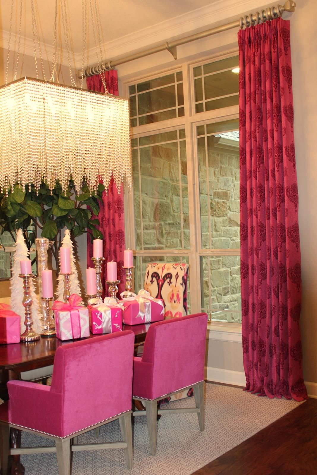 A dining room with pink chairs , a table and a chandelier.