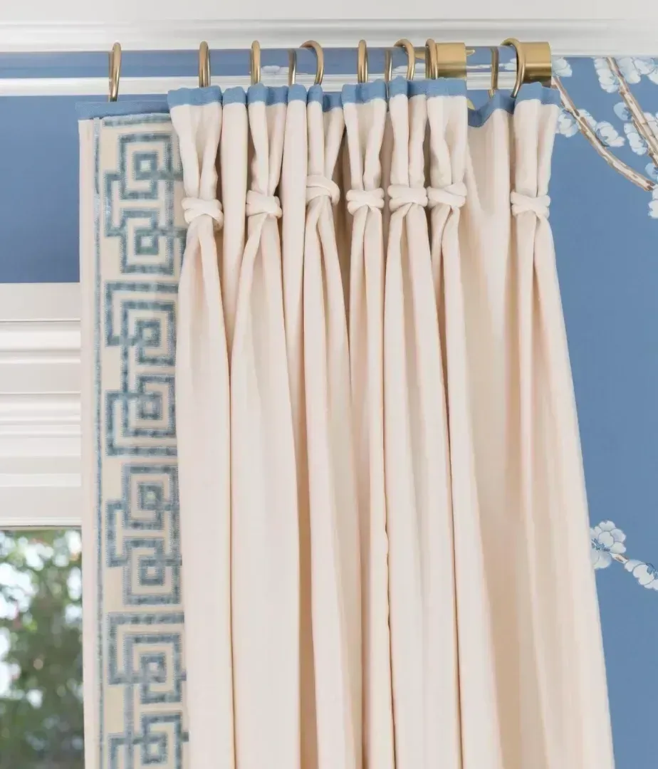 A pair of white curtains with a blue greek key trim