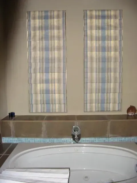 A bathroom with a bathtub and two windows with plaid curtains