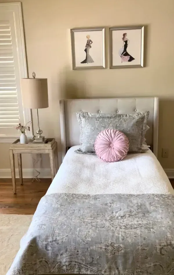 A bedroom with a single bed , a lamp , and two pictures on the wall.