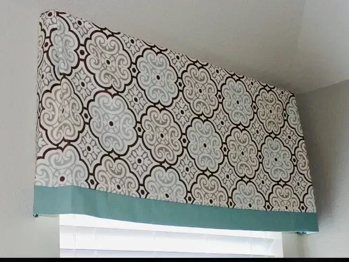 A window valance with a pattern on it is hanging from the ceiling above a window.