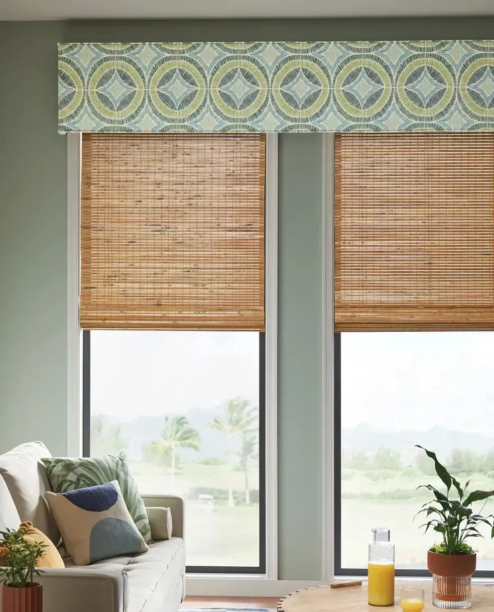 A living room with a couch , table , and two windows with bamboo blinds.