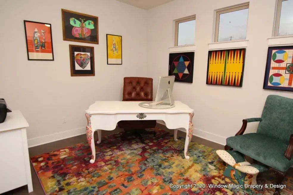 A home office with a desk , chair , and paintings on the wall.
